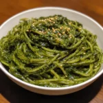 A plate of green spaghetti garnished with fresh basil leaves and grated parmesan cheese.